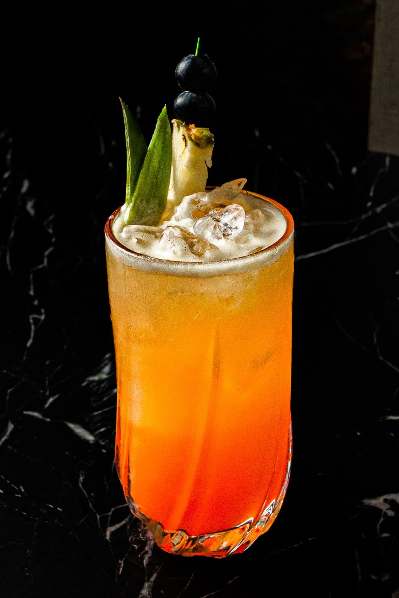 Orange drink in a tall glass with pineapple and blueberries