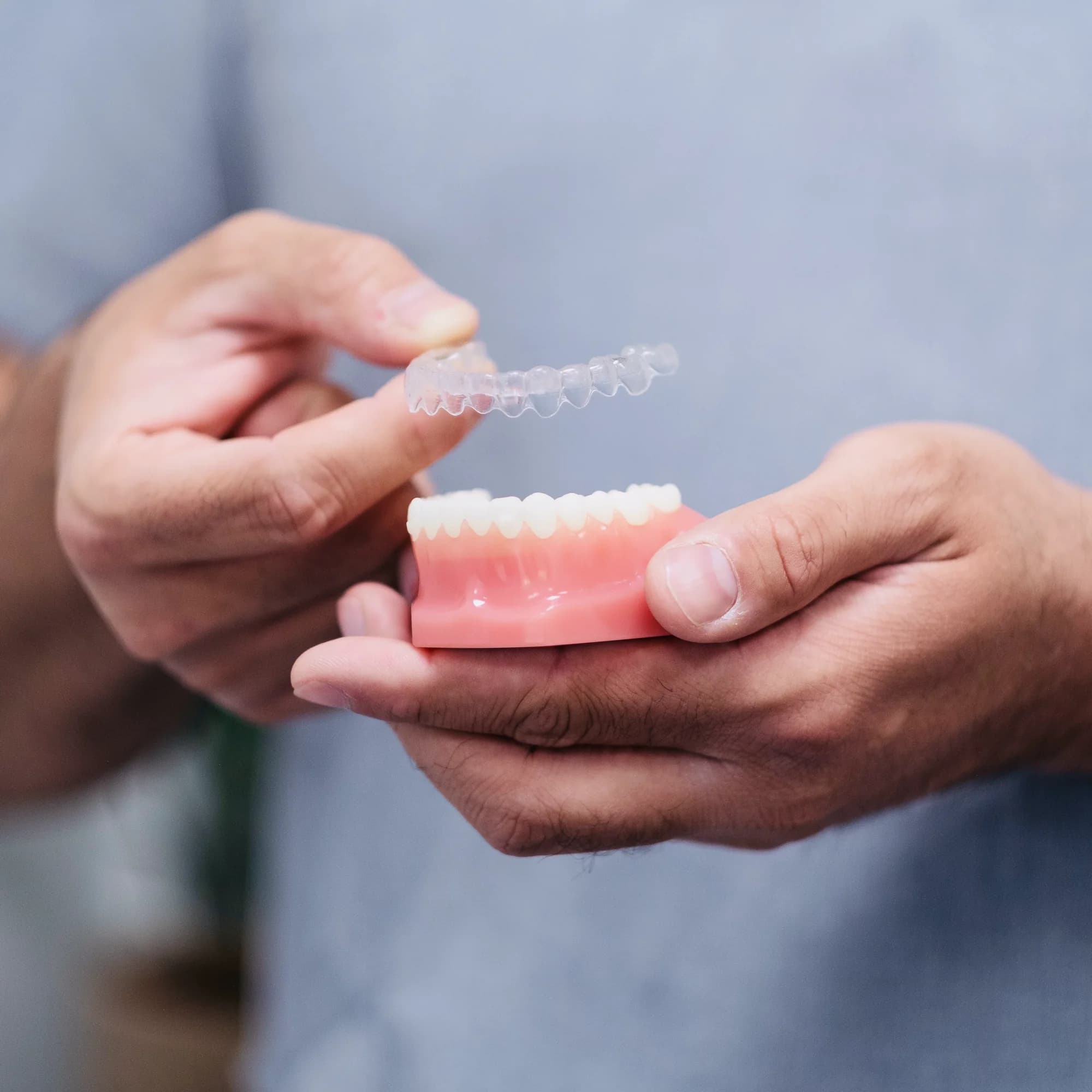 Hands holding a clear aligner over a dental model