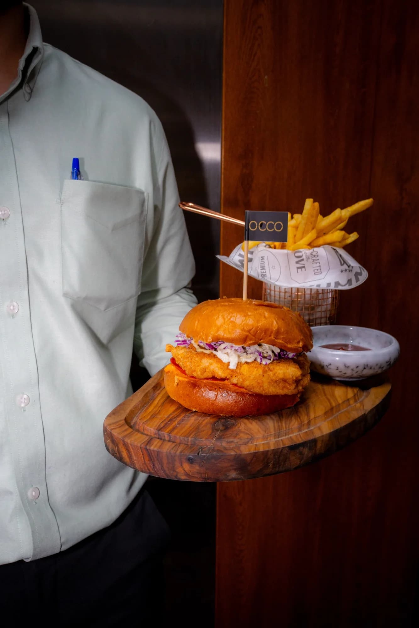 Waiter carrying a burger and fries on a wooden board